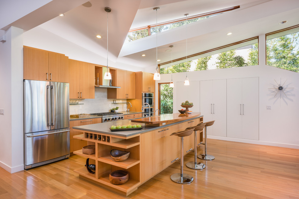 サンフランシスコにあるコンテンポラリースタイルのおしゃれなアイランドキッチン (フラットパネル扉のキャビネット、中間色木目調キャビネット、白いキッチンパネル、シルバーの調理設備、淡色無垢フローリング) の写真