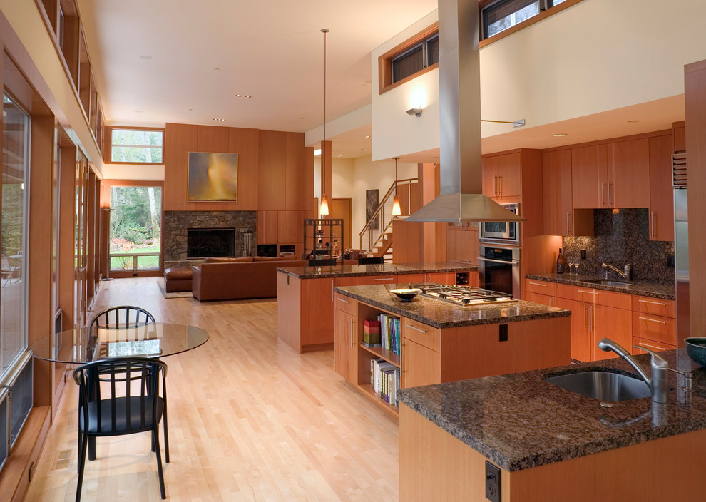 Contemporary u-shaped open plan kitchen in Seattle with a single-bowl sink, flat-panel cabinets, medium wood cabinets, granite worktops, stone tiled splashback, stainless steel appliances, light hardwood flooring and an island.