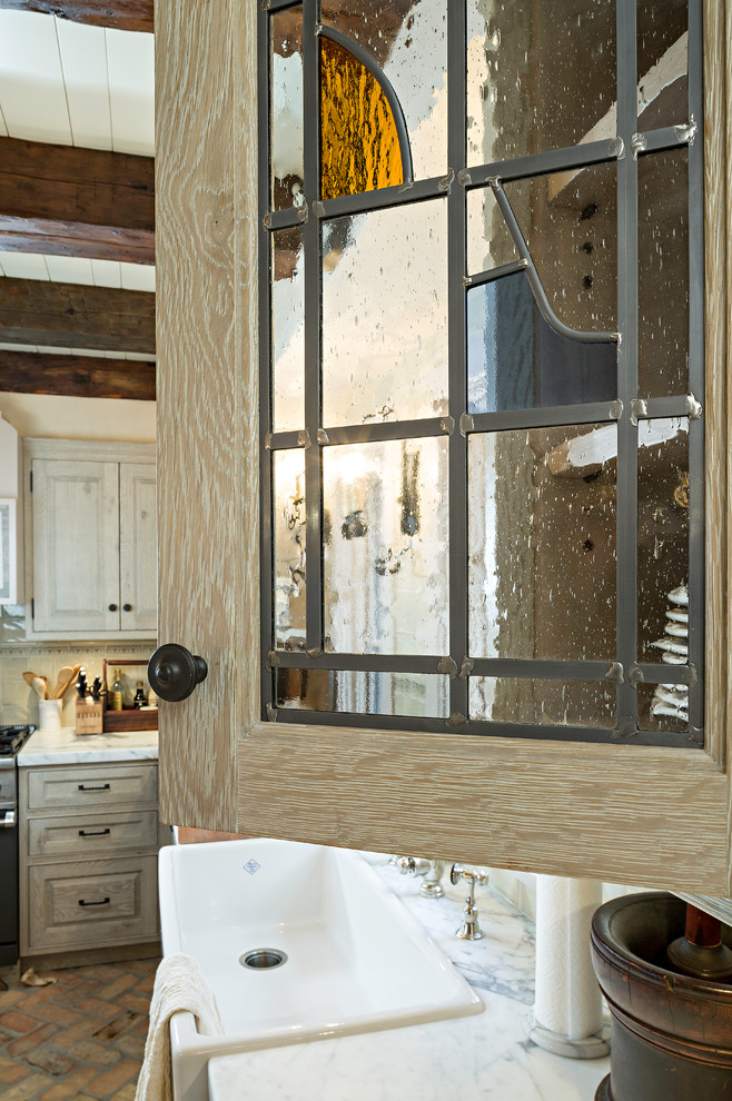 Foto på ett avskilt, mellanstort lantligt u-kök, med en rustik diskho, luckor med upphöjd panel, skåp i slitet trä, marmorbänkskiva, beige stänkskydd, stänkskydd i keramik, integrerade vitvaror, tegelgolv och en köksö
