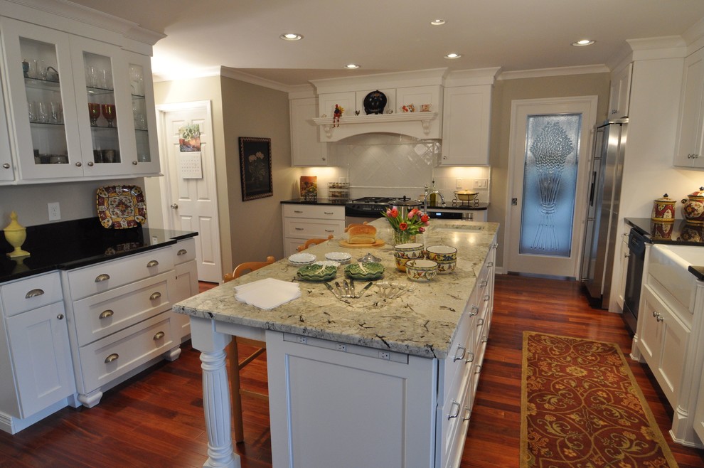 Klassisk inredning av ett avskilt, stort u-kök, med en rustik diskho, skåp i shakerstil, vita skåp, granitbänkskiva, vitt stänkskydd, stänkskydd i keramik, rostfria vitvaror, mellanmörkt trägolv och en köksö