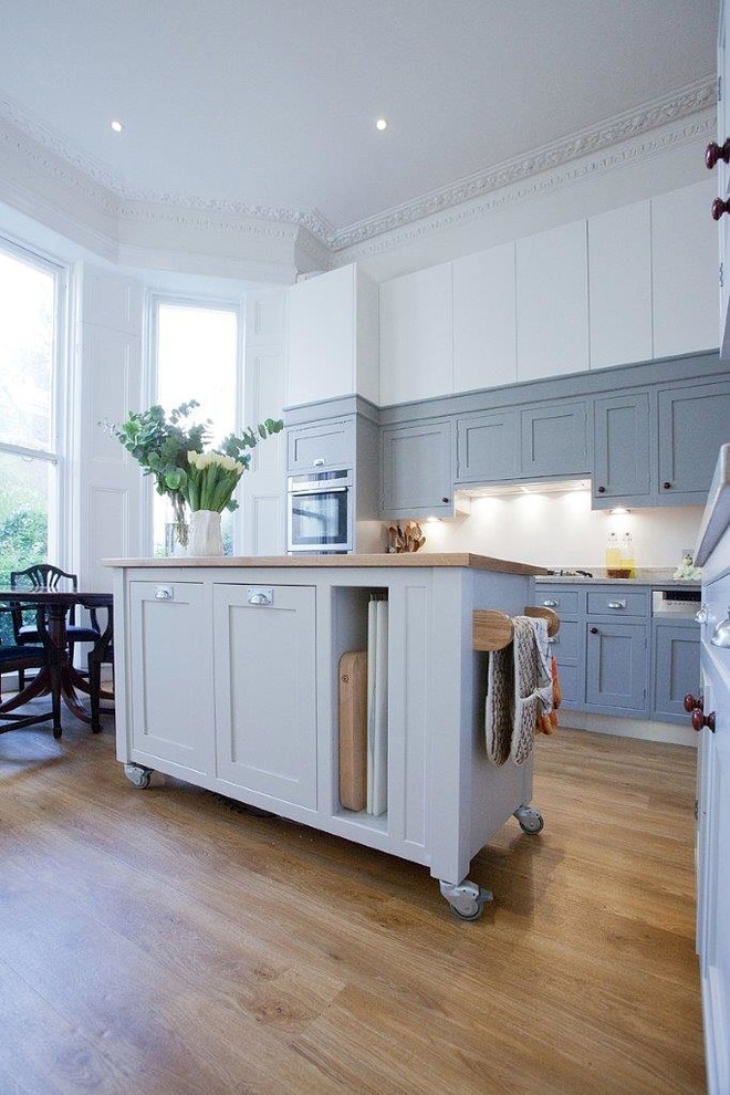 This is an example of a medium sized traditional kitchen in London with blue cabinets, stainless steel appliances and an island.