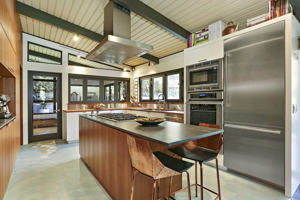 Retro u-shaped kitchen in Los Angeles with a submerged sink, flat-panel cabinets, medium wood cabinets, grey splashback, metal splashback, stainless steel appliances, an island, green floors and black worktops.