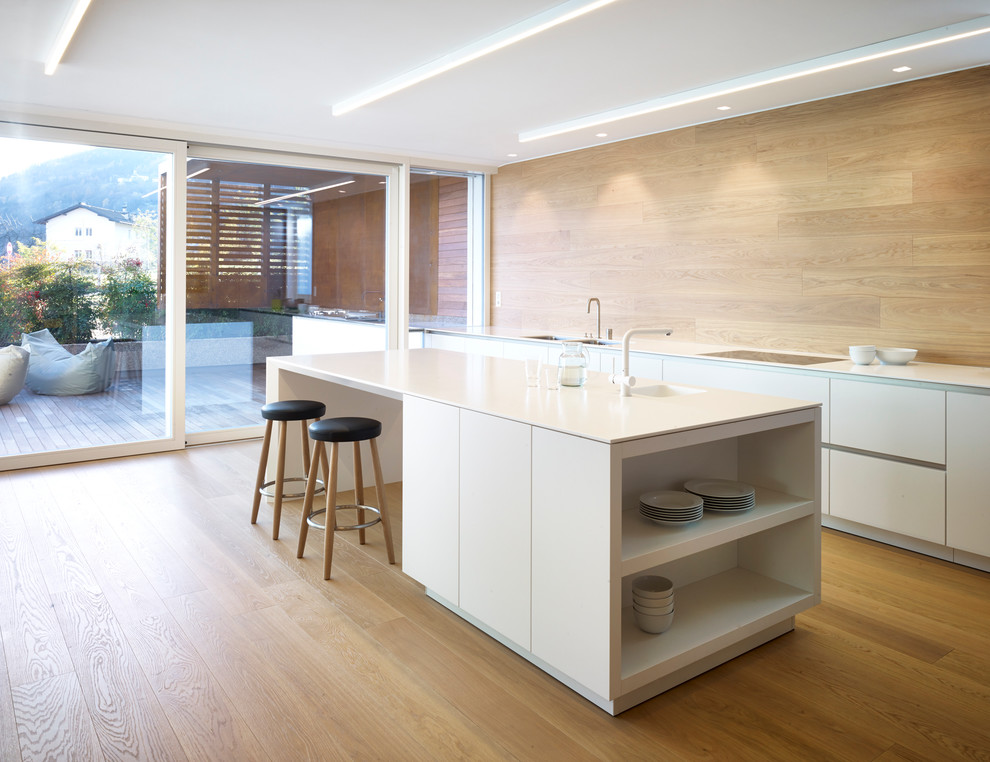 Zweizeilige Moderne Küche mit flächenbündigen Schrankfronten, weißen Schränken, hellem Holzboden, Kücheninsel und Küchenrückwand in Braun in Sonstige