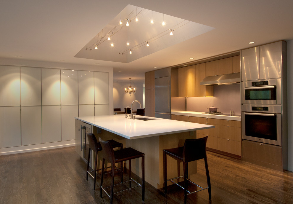 Photo of a large modern single-wall open plan kitchen in Seattle with a built-in sink, flat-panel cabinets, light wood cabinets, granite worktops, beige splashback, stainless steel appliances, medium hardwood flooring and an island.