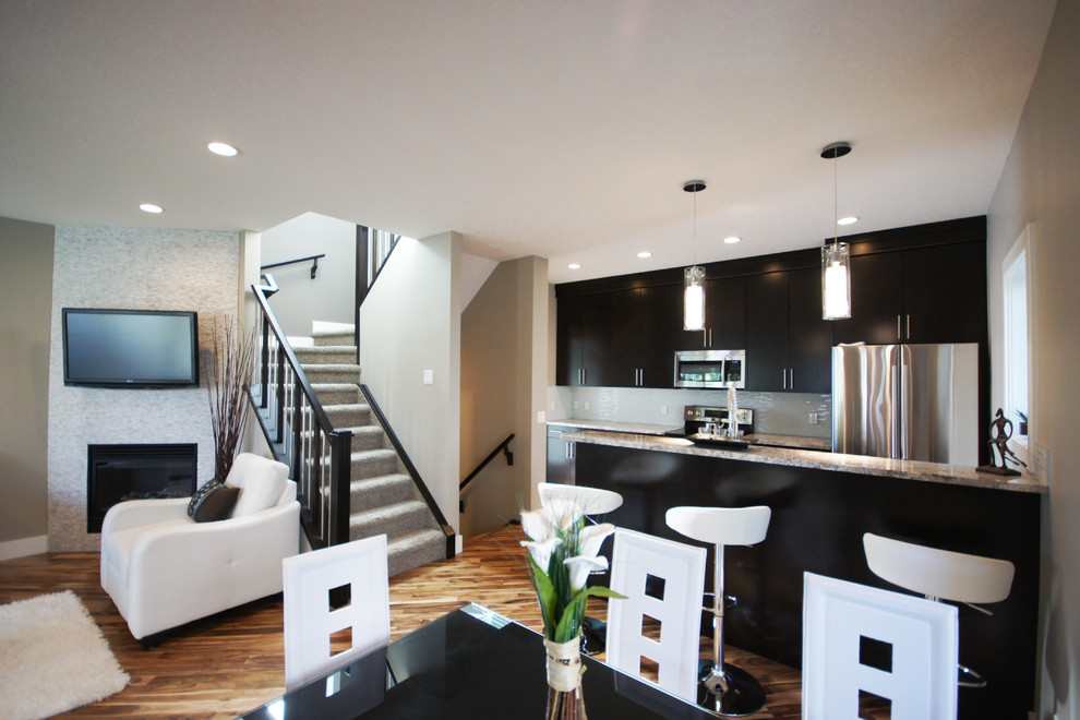 Идея дизайна: кухня-гостиная в современном стиле с двойной мойкой, плоскими фасадами, темными деревянными фасадами, гранитной столешницей, белым фартуком и техникой из нержавеющей стали