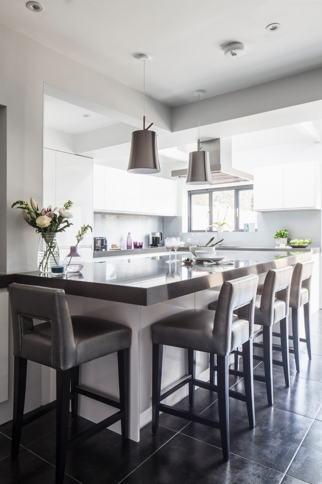 This is an example of a medium sized contemporary l-shaped kitchen/diner in Sussex with white cabinets, engineered stone countertops, black appliances, a breakfast bar and grey worktops.