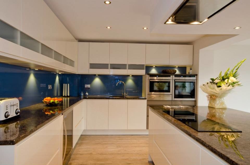 This is an example of a large modern kitchen in Kent with a single-bowl sink, flat-panel cabinets, light wood cabinets, granite worktops, blue splashback, glass tiled splashback, stainless steel appliances and an island.