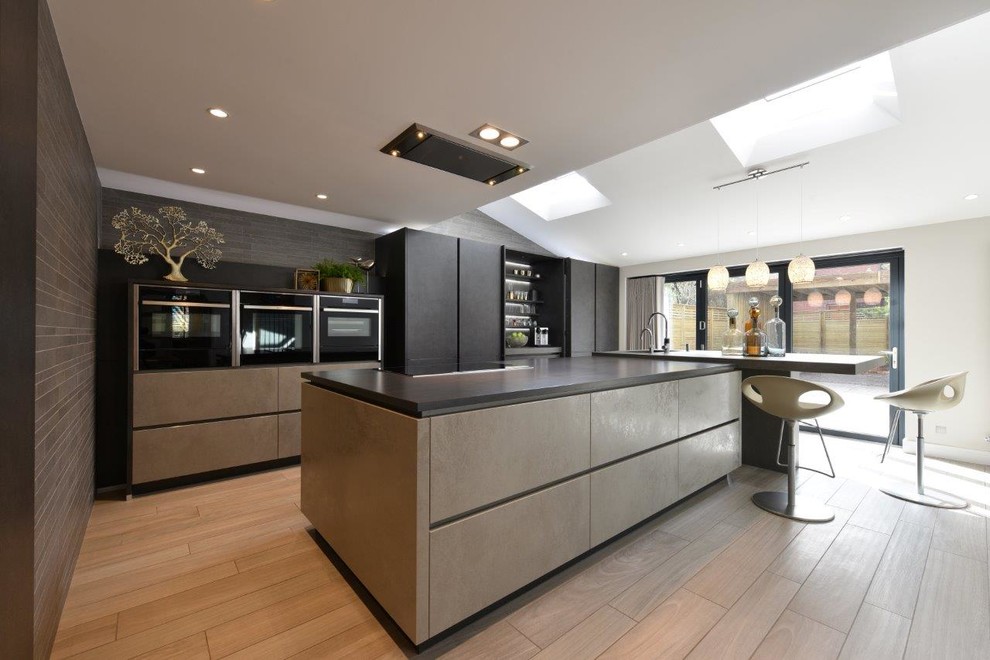 Inspiration for a large contemporary galley kitchen in Manchester with a double-bowl sink, flat-panel cabinets, grey cabinets, engineered stone countertops, grey splashback, glass sheet splashback, stainless steel appliances, porcelain flooring and an island.