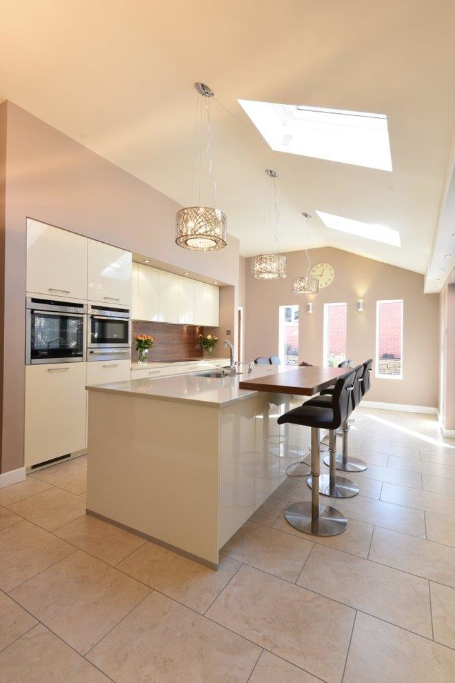Inspiration for a medium sized contemporary open plan kitchen in Manchester with a built-in sink, flat-panel cabinets, beige cabinets, quartz worktops, brown splashback, stainless steel appliances, ceramic flooring and an island.