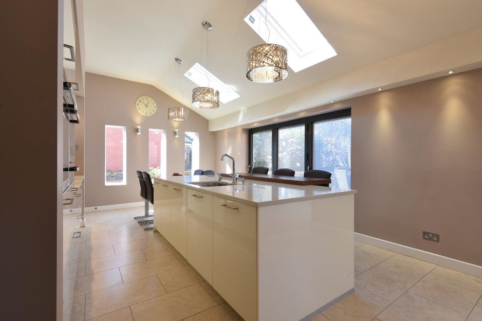Medium sized contemporary open plan kitchen in Manchester with a built-in sink, flat-panel cabinets, beige cabinets, quartz worktops, brown splashback, stainless steel appliances, ceramic flooring and an island.