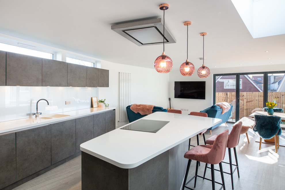 Design ideas for a medium sized contemporary l-shaped open plan kitchen in Other with an integrated sink, flat-panel cabinets, grey cabinets, composite countertops, white splashback, glass sheet splashback, black appliances, an island and white worktops.