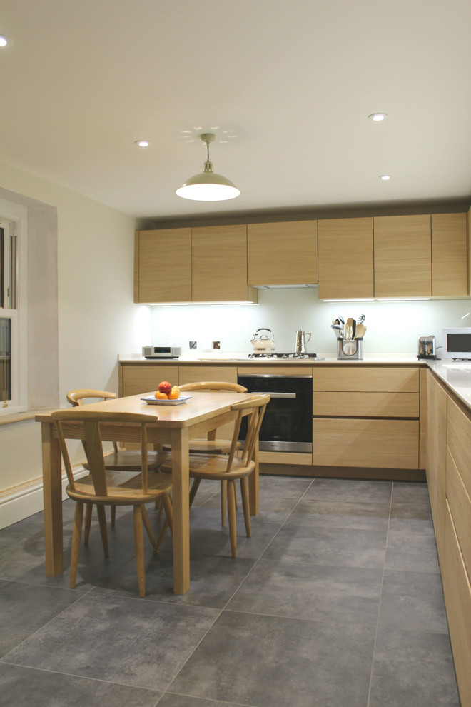 Moderne Wohnküche ohne Insel in L-Form mit integriertem Waschbecken, flächenbündigen Schrankfronten, hellen Holzschränken, Glasrückwand und Elektrogeräten mit Frontblende in Wiltshire