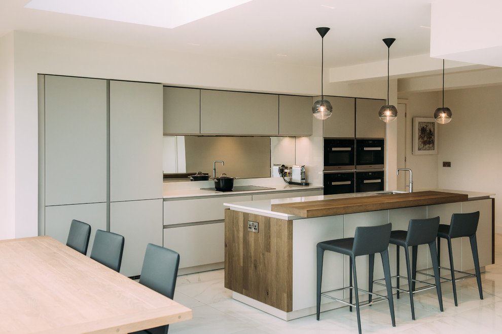 Design ideas for a contemporary galley kitchen/diner in Cheshire with a submerged sink, flat-panel cabinets, grey cabinets, metallic splashback, mirror splashback, integrated appliances, marble flooring, an island, white floors and white worktops.