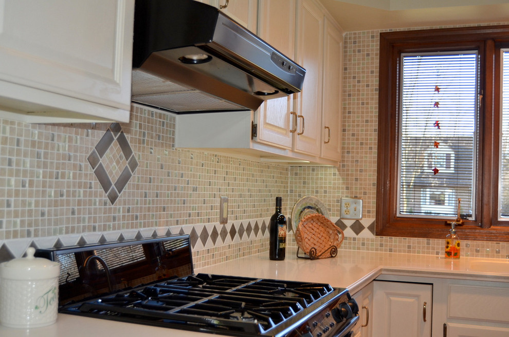 Example of a mid-sized classic u-shaped medium tone wood floor and brown floor kitchen design in Detroit with an undermount sink, raised-panel cabinets, white cabinets, multicolored backsplash, mosaic tile backsplash, black appliances and an island