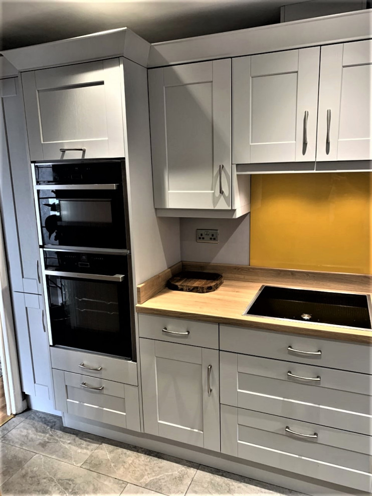 Inspiration for a medium sized classic u-shaped enclosed kitchen in Other with shaker cabinets, grey cabinets, yellow splashback, glass sheet splashback, black appliances, porcelain flooring, no island and grey floors.