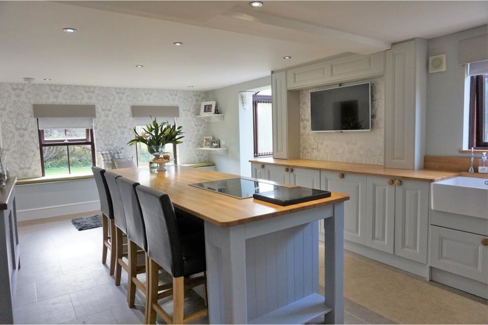 Inspiration for a large traditional galley enclosed kitchen in Cornwall with a belfast sink, raised-panel cabinets, blue cabinets, wood worktops, wood splashback, stainless steel appliances, vinyl flooring and an island.