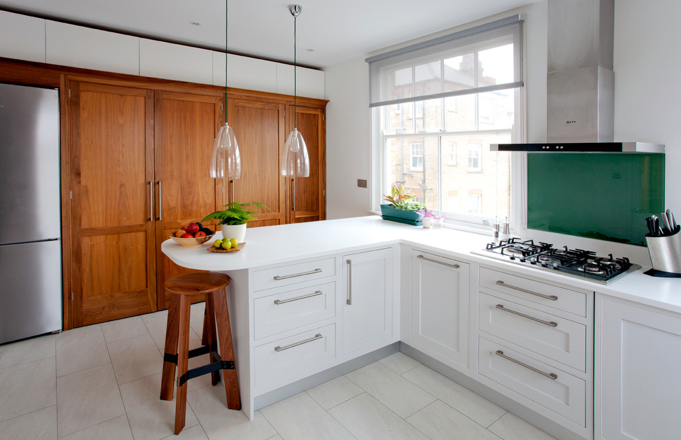 Foto på ett litet funkis l-kök, med skåp i shakerstil, vita skåp, grönt stänkskydd, rostfria vitvaror och en halv köksö