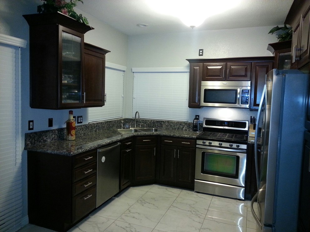 Klassische Küche in U-Form mit Doppelwaschbecken, profilierten Schrankfronten, dunklen Holzschränken, Granit-Arbeitsplatte, weißen Elektrogeräten und hellem Holzboden in Las Vegas