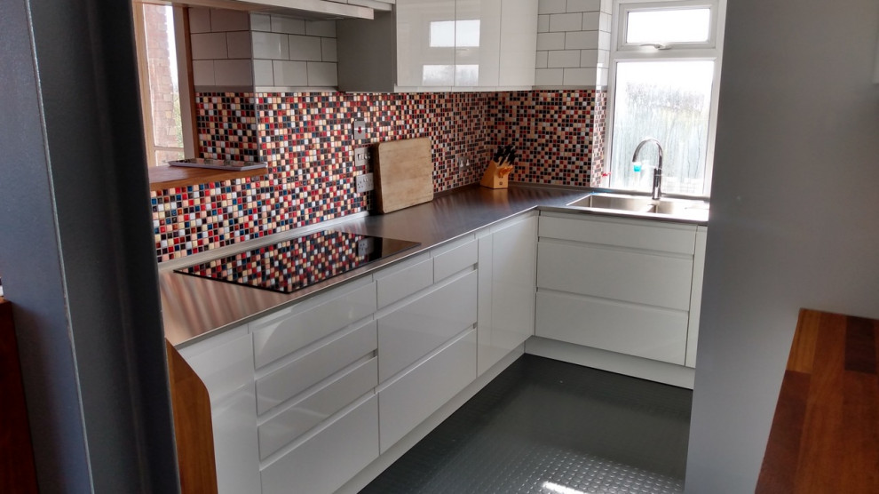 Geschlossene Moderne Küche in U-Form mit integriertem Waschbecken, flächenbündigen Schrankfronten, weißen Schränken und Edelstahl-Arbeitsplatte in Hertfordshire