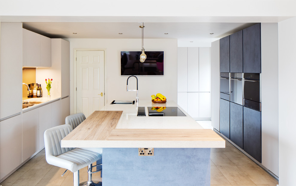 This is an example of a medium sized contemporary galley kitchen in Edinburgh with flat-panel cabinets, stainless steel appliances, an island, beige floors, wood worktops and white cabinets.