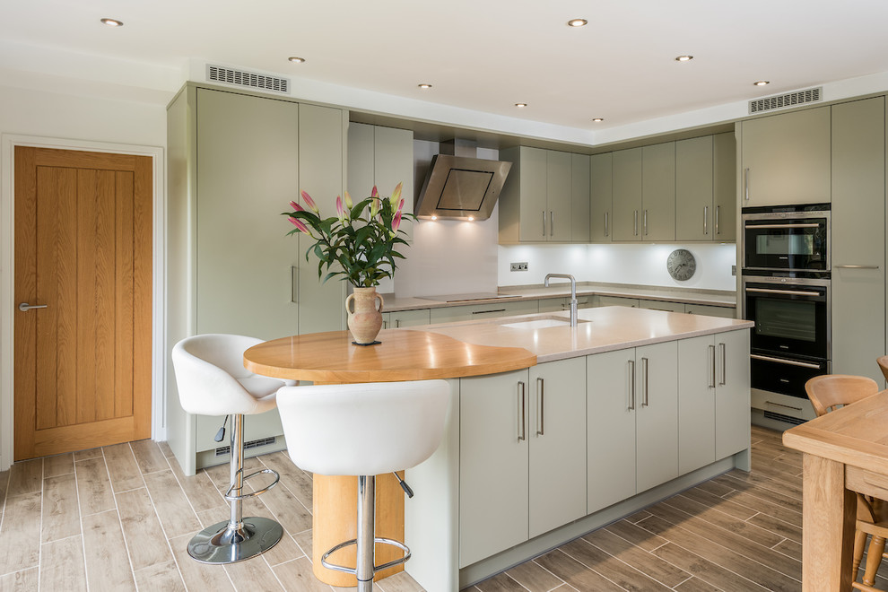Contemporary l-shaped kitchen/diner in Other with a submerged sink, flat-panel cabinets, green cabinets, white splashback, black appliances, an island, brown floors and grey worktops.