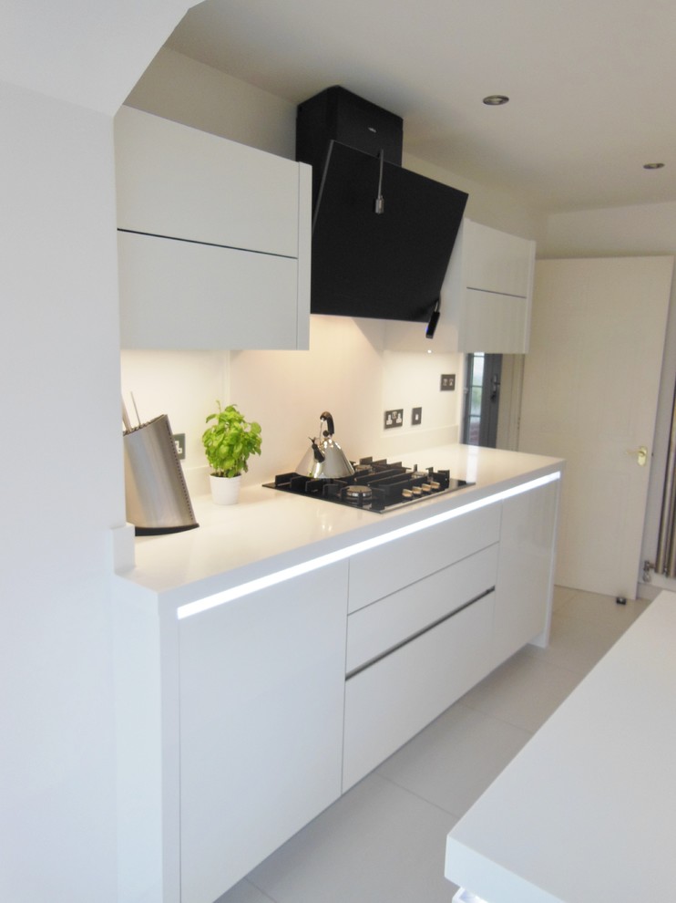 Modern inredning av ett mellanstort kök, med en enkel diskho, släta luckor, vita skåp, vitt stänkskydd, glaspanel som stänkskydd, rostfria vitvaror, klinkergolv i porslin och en halv köksö