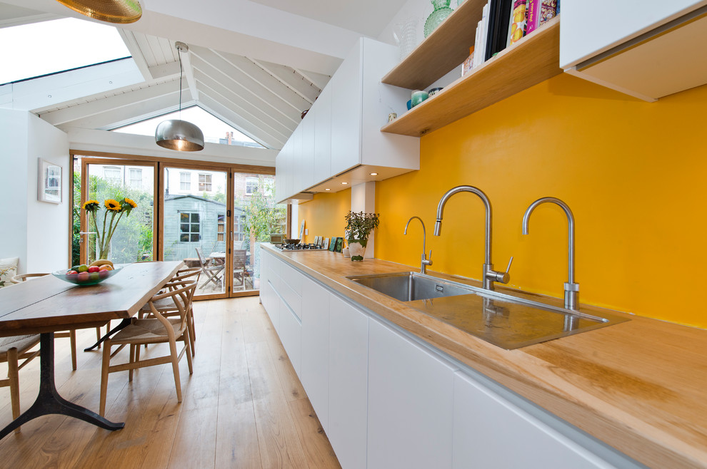 Example of a mid-sized trendy medium tone wood floor and beige floor eat-in kitchen design in London with a double-bowl sink, flat-panel cabinets, white cabinets, wood countertops, colored appliances and no island