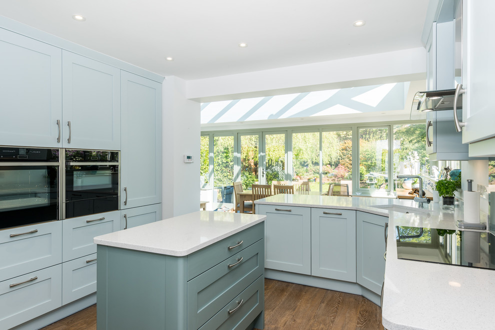 This is an example of a nautical kitchen in Other with a submerged sink, shaker cabinets, blue cabinets, black appliances, medium hardwood flooring, an island and white worktops.