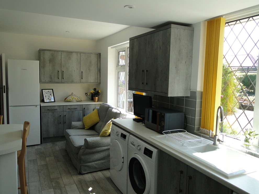 Medium sized contemporary l-shaped enclosed kitchen in Other with a double-bowl sink, flat-panel cabinets, grey cabinets, laminate countertops, grey splashback, ceramic splashback, ceramic flooring, grey floors and white worktops.