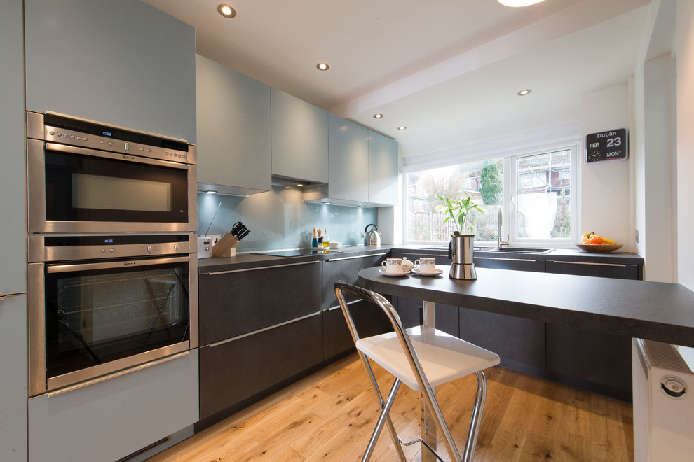 Foto di una piccola cucina a L moderna con ante lisce, ante blu, paraspruzzi blu, paraspruzzi con lastra di vetro, elettrodomestici in acciaio inossidabile e penisola