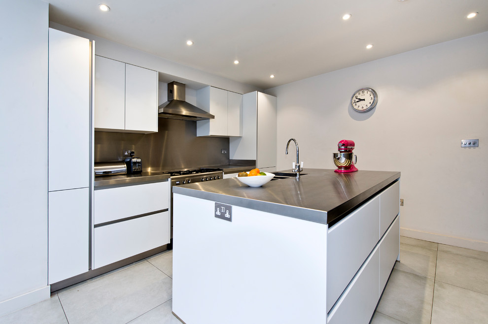 Mittelgroße Moderne Wohnküche mit integriertem Waschbecken, flächenbündigen Schrankfronten, weißen Schränken, Edelstahl-Arbeitsplatte, Küchenrückwand in Metallic, Küchengeräten aus Edelstahl und Kücheninsel in London