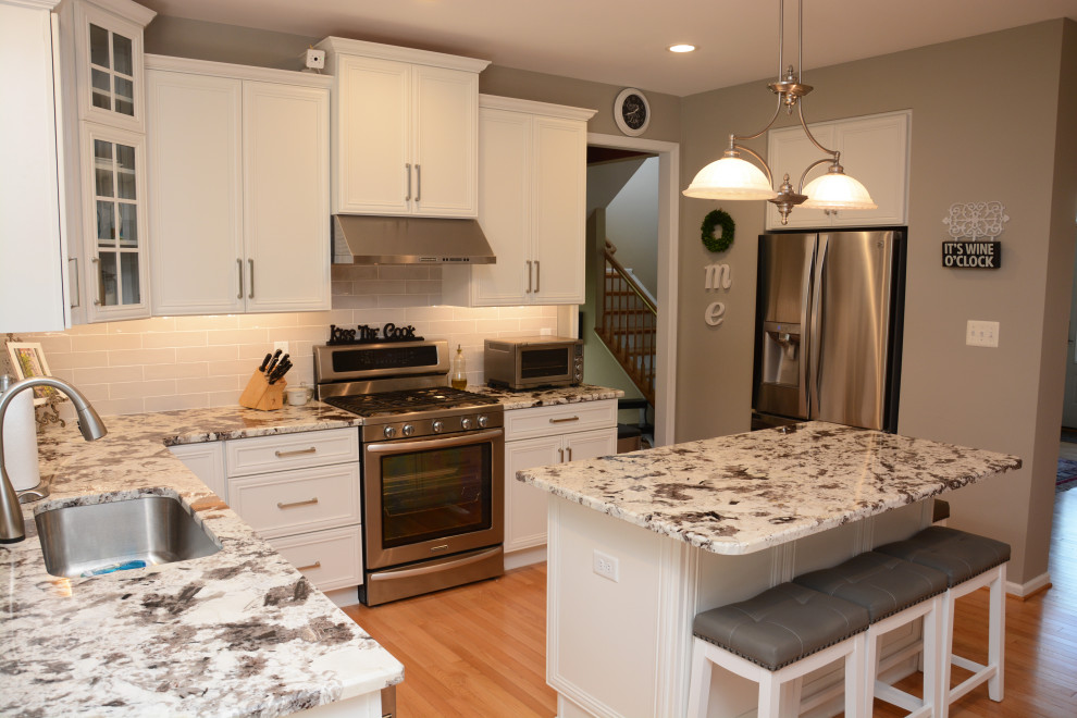 Example of a mid-sized classic u-shaped light wood floor and brown floor open concept kitchen design in DC Metro with an undermount sink, recessed-panel cabinets, white cabinets, granite countertops, gray backsplash, stainless steel appliances, an island and white countertops