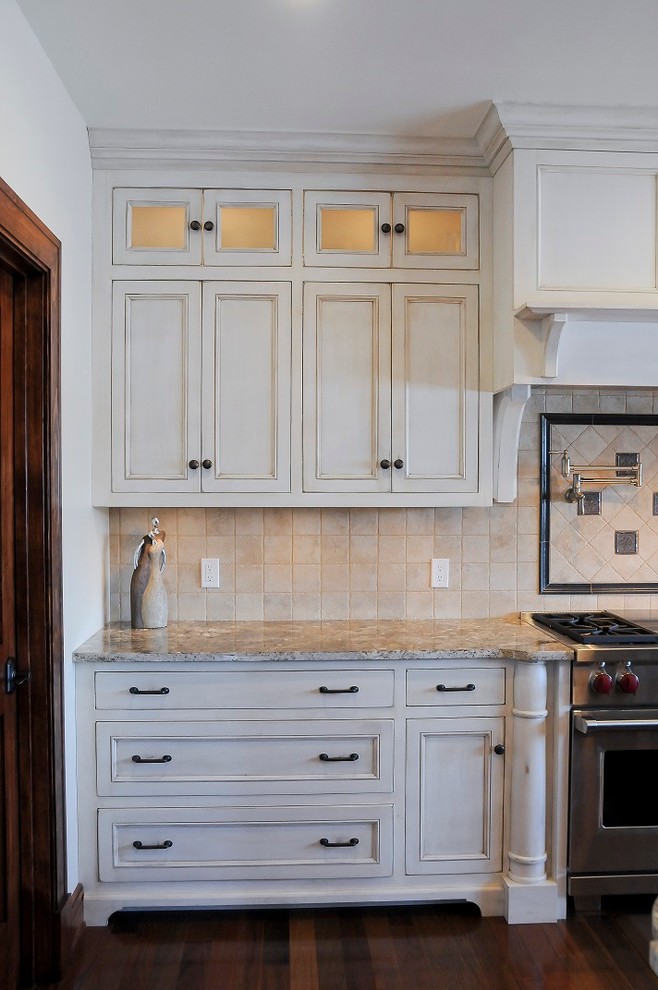 Cette photo montre une cuisine américaine craftsman en L et bois vieilli de taille moyenne avec un évier encastré, un placard avec porte à panneau encastré, un plan de travail en granite, une crédence beige, un électroménager en acier inoxydable, un sol en bois brun et îlot.