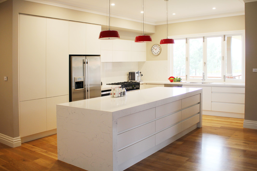 Modern inredning av ett stort kök, med bänkskiva i glas, vitt stänkskydd, ljust trägolv och en köksö