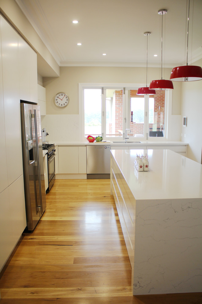 Imagen de cocina minimalista grande con salpicadero blanco, suelo de madera clara y una isla