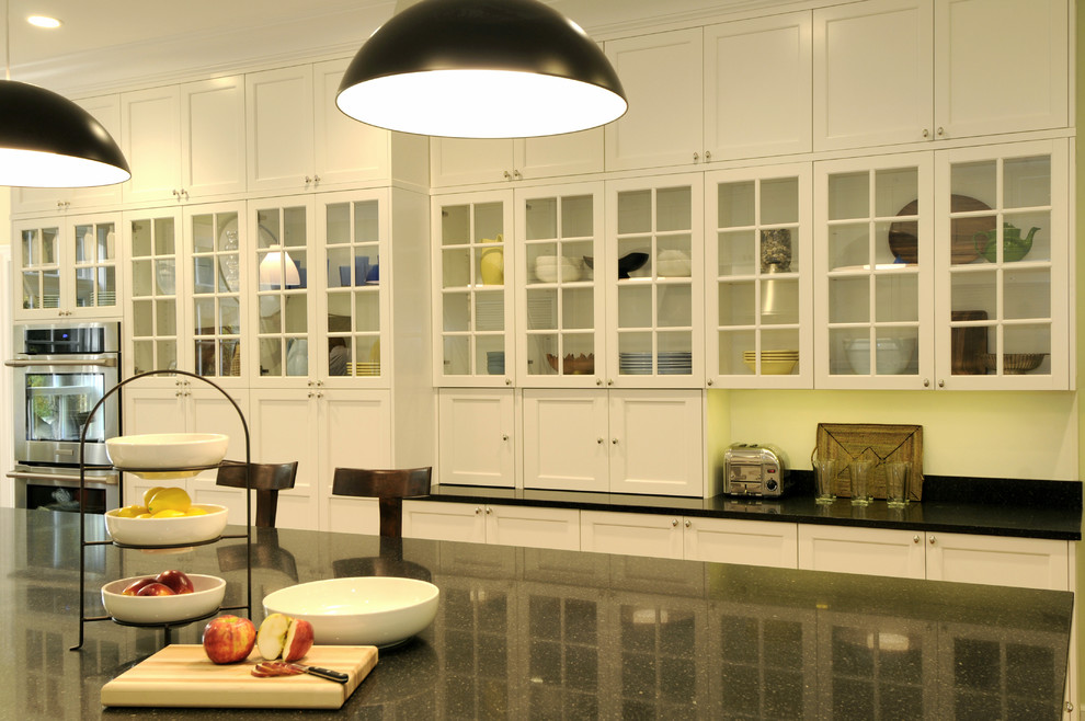 Example of a large transitional galley kitchen design in New York with flat-panel cabinets, white cabinets, quartz countertops, black backsplash, stainless steel appliances and an island