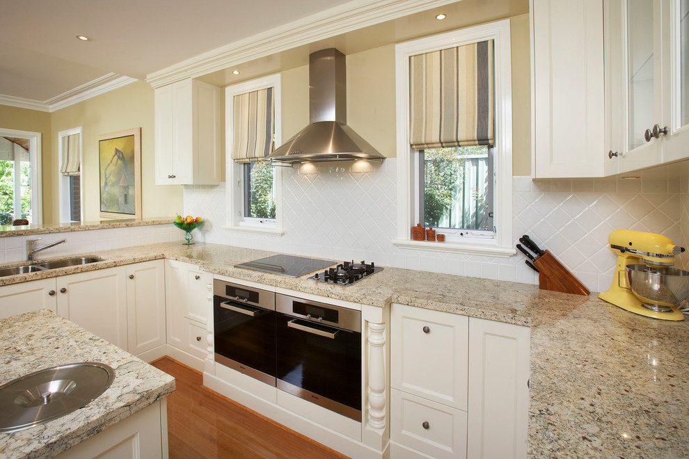 Foto på ett vintage flerfärgad kök, med en undermonterad diskho, skåp i shakerstil, vita skåp, granitbänkskiva, vitt stänkskydd, stänkskydd i porslinskakel, rostfria vitvaror och en köksö