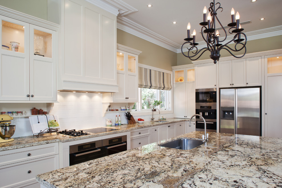 Exempel på ett klassiskt flerfärgad flerfärgat kök, med en undermonterad diskho, skåp i shakerstil, vita skåp, granitbänkskiva, vitt stänkskydd, rostfria vitvaror, en köksö och stänkskydd i tunnelbanekakel