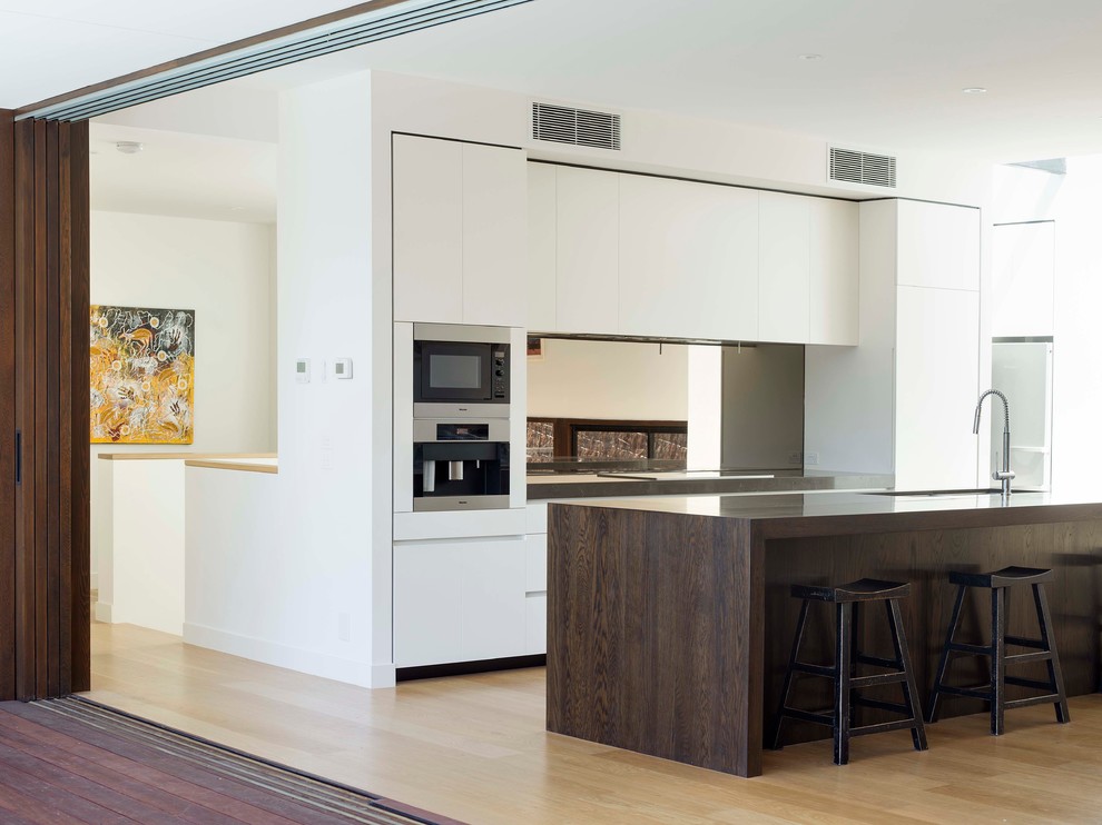 Exempel på ett stort modernt kök, med en undermonterad diskho, släta luckor, skåp i mörkt trä, marmorbänkskiva, stänkskydd med metallisk yta, spegel som stänkskydd, rostfria vitvaror, ljust trägolv och en köksö