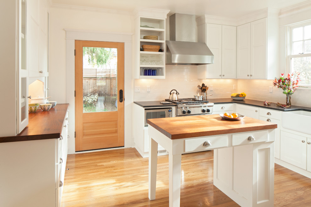 ポートランドにあるトラディショナルスタイルのおしゃれなキッチン (エプロンフロントシンク、落し込みパネル扉のキャビネット、白いキャビネット、木材カウンター、白いキッチンパネル、サブウェイタイルのキッチンパネル、シルバーの調理設備、無垢フローリング) の写真
