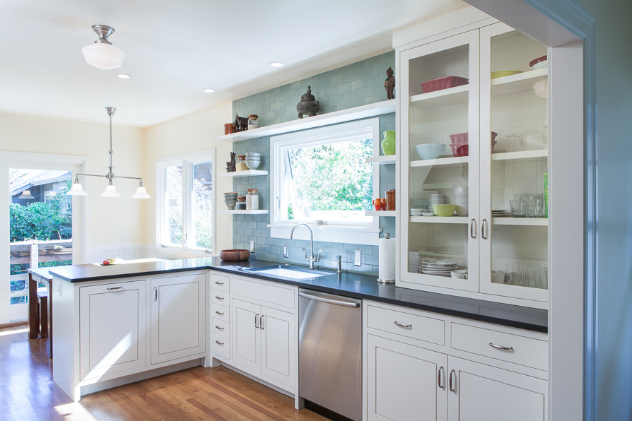 Klassische Wohnküche in L-Form mit Unterbauwaschbecken, weißen Schränken, Glasfronten, Küchenrückwand in Blau, Rückwand aus Keramikfliesen, Küchengeräten aus Edelstahl und Granit-Arbeitsplatte in Portland