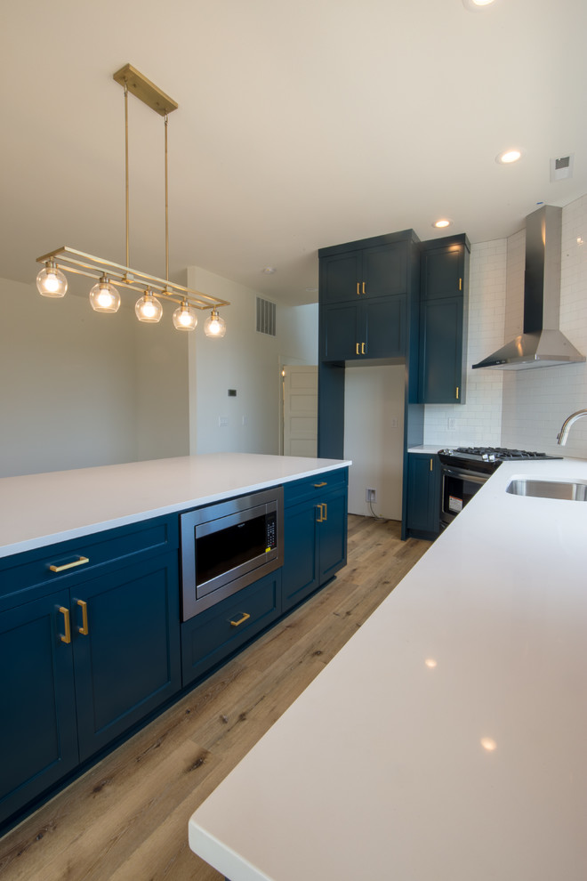 Idéer för att renovera ett mellanstort funkis vit vitt kök, med en integrerad diskho, luckor med infälld panel, blå skåp, vitt stänkskydd, stänkskydd i keramik, rostfria vitvaror, ljust trägolv, en köksö och brunt golv