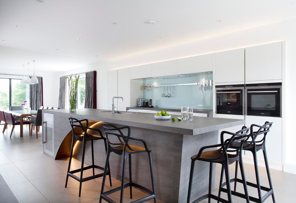 Bild på ett mycket stort funkis kök, med en integrerad diskho, släta luckor, vita skåp, bänkskiva i kvarts, grönt stänkskydd, glaspanel som stänkskydd, rostfria vitvaror, klinkergolv i keramik och en köksö