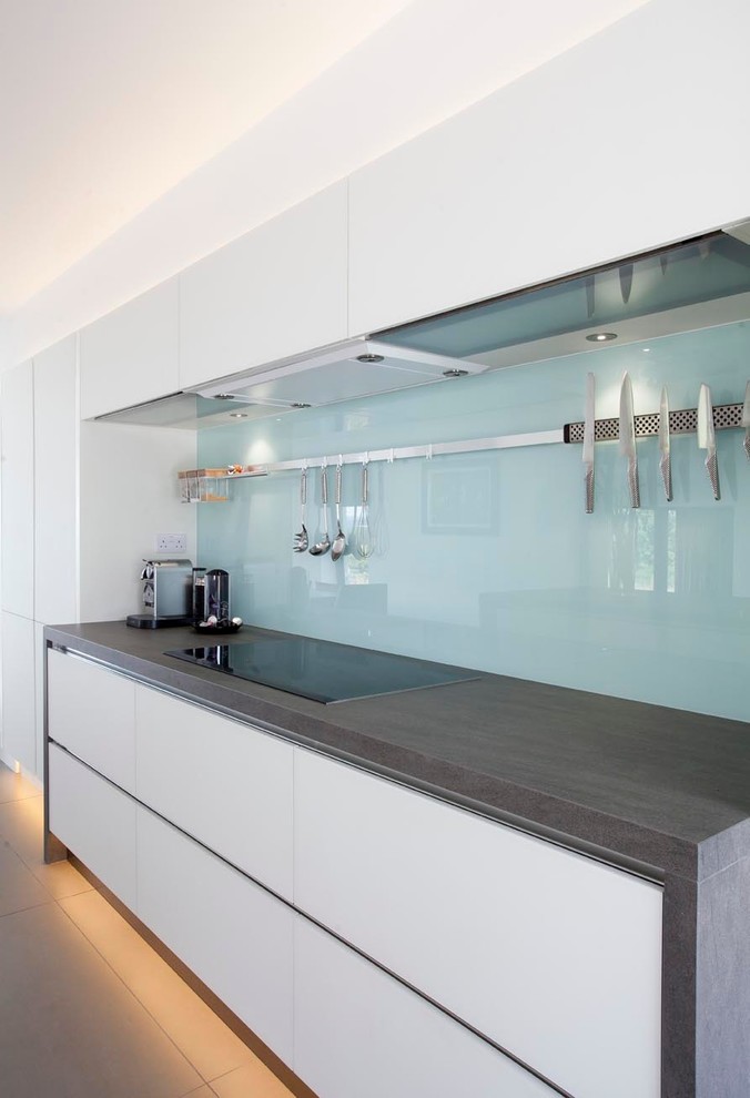 Expansive contemporary u-shaped open plan kitchen in Other with an integrated sink, flat-panel cabinets, white cabinets, engineered stone countertops, green splashback, glass sheet splashback, stainless steel appliances, ceramic flooring and an island.