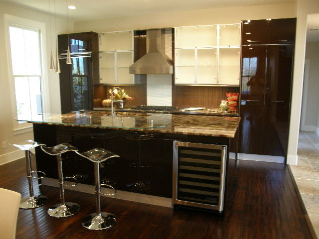 Cette image montre une cuisine américaine linéaire design avec un évier encastré, un placard à porte vitrée, un plan de travail en quartz modifié, une crédence marron et un électroménager en acier inoxydable.