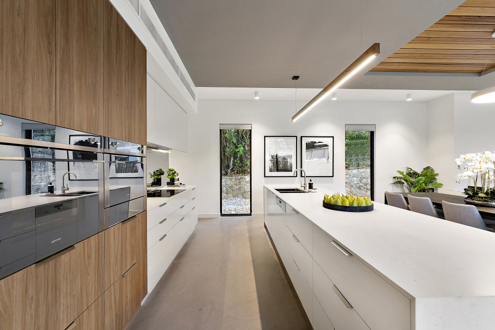 Mid-sized trendy single-wall concrete floor and gray floor eat-in kitchen photo in Canberra - Queanbeyan with an undermount sink, flat-panel cabinets, white cabinets, quartz countertops, metallic backsplash, mirror backsplash, black appliances, an island and white countertops