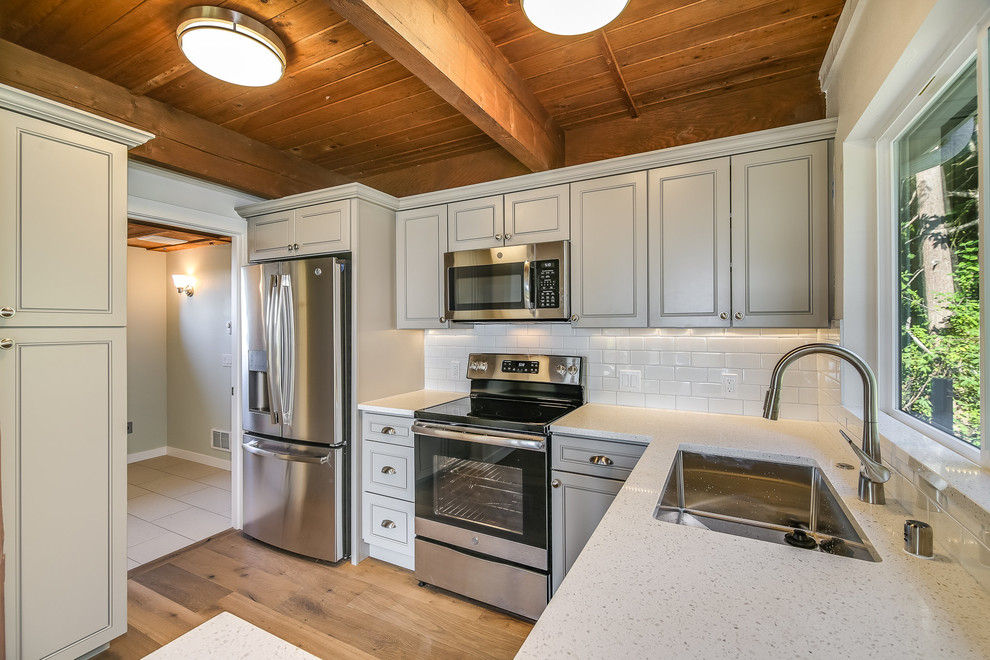 Small beach style u-shaped light wood floor and brown floor eat-in kitchen photo in Seattle with an undermount sink, raised-panel cabinets, gray cabinets, quartz countertops, white backsplash, ceramic backsplash, stainless steel appliances, a peninsula and white countertops