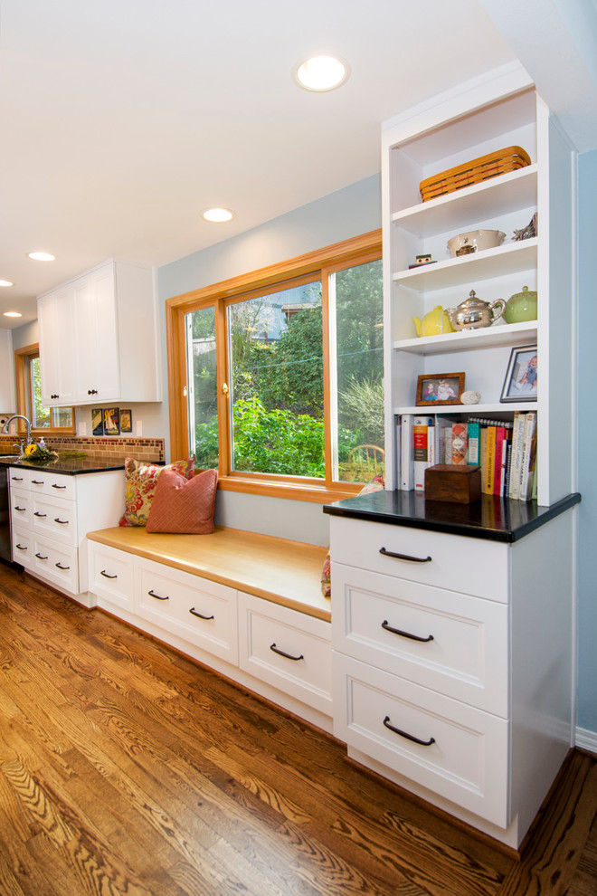 Inspiration for a mid-sized cottage l-shaped medium tone wood floor eat-in kitchen remodel in Seattle with a farmhouse sink, recessed-panel cabinets, white cabinets, soapstone countertops, beige backsplash, ceramic backsplash, stainless steel appliances and an island