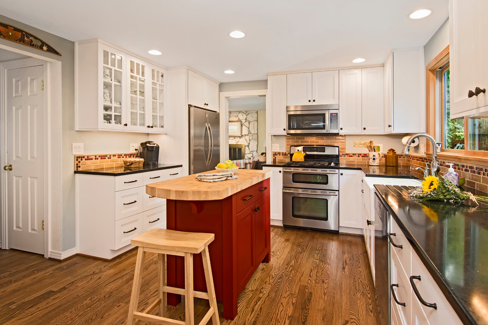 Bild på ett mellanstort lantligt kök, med en rustik diskho, luckor med infälld panel, vita skåp, bänkskiva i täljsten, beige stänkskydd, stänkskydd i keramik, rostfria vitvaror, mellanmörkt trägolv och en köksö