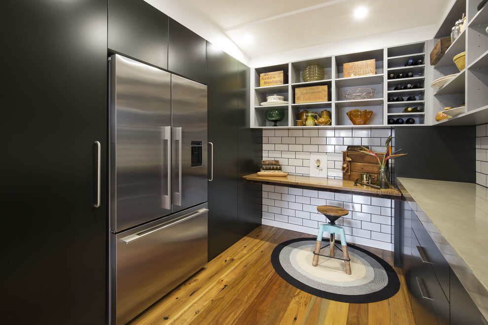Bild på ett mellanstort funkis linjärt kök med öppen planlösning, med en undermonterad diskho, släta luckor, svarta skåp, bänkskiva i betong, svart stänkskydd, stänkskydd i metallkakel, rostfria vitvaror, mellanmörkt trägolv och en köksö